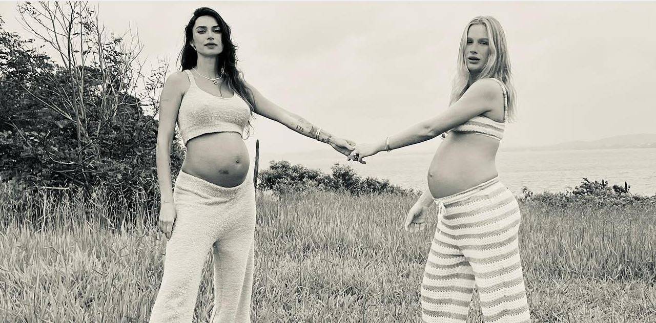 duas mulheres grávidas, com roupas que mostram a barriga, em uma campo. Elas estão com uma das mãos dadas