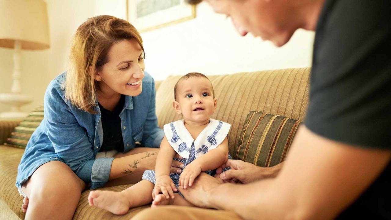 homem e mulher sentados com uma bebê em um sofá. A criança olha para o homem e dá um leve sorriso