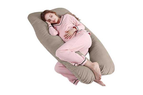 mulher grávida usando pijama deitada em um travesseiro grande em formato de U