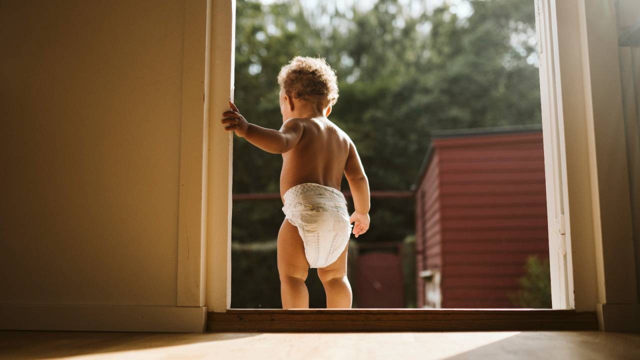 bebê de fralda em pé ao lado da porta