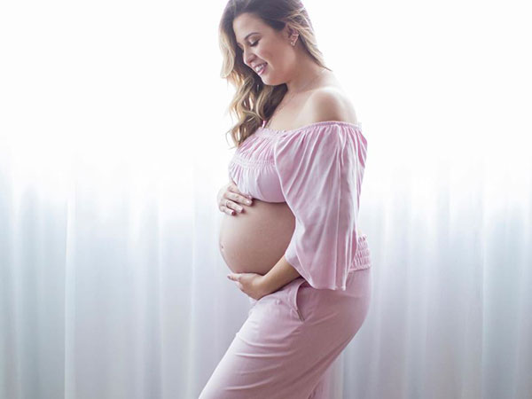 fabi-santina-entrevista-gravidez mulher gravida, diante de uma cortina branca. Ela está em pé, de lado e com as mãos na barriga