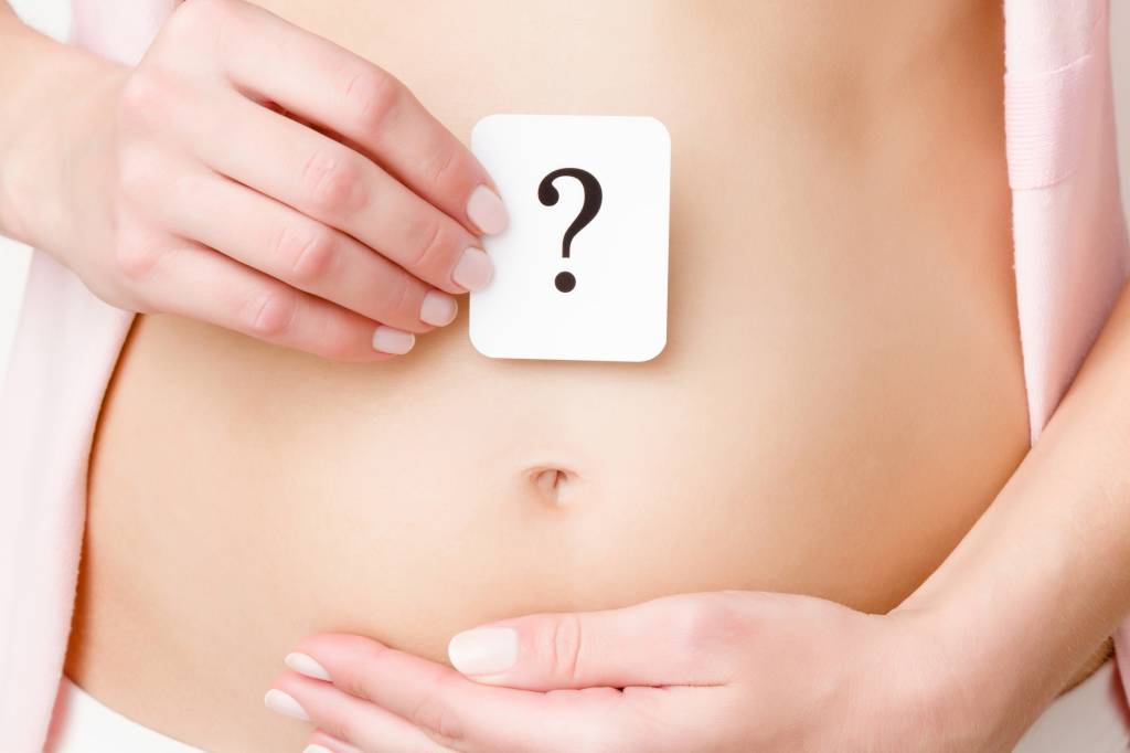 barriga de grávida barriga de grávida ainda pequena. Está com as duas mãos sobre ela, uma delas segura um cartão com um ponto de interrogação.