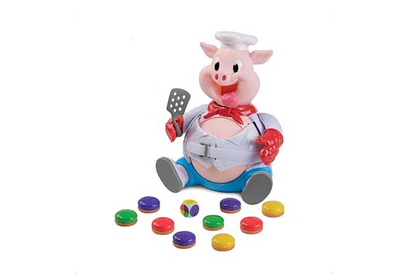 porco de brinquedo usando roupas de cozinheiro. Na frete dele, há algumas peças coloridas