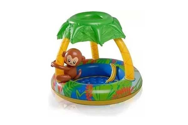 piscina infantil inflável, redonda e com cobertura que imita o desenho de uma palmeira. Um macaco, também plástico, está abraçado a um dos galhos