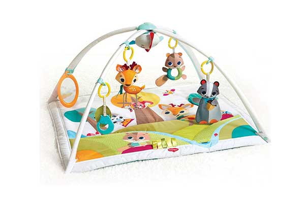 Tapete de atividades infantil em formato quadrado. Ele é colorido e tem ilustrações de animais. Acima, há dois arcos transversais, onde estão pendurados brinquedos.