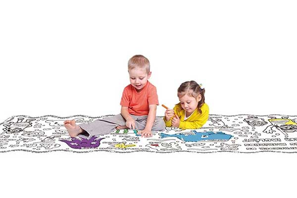 Duas crianças brincando sobre um tapete retangular cheio de ilustrações em preto e branco. Algumas delas estão pintadas