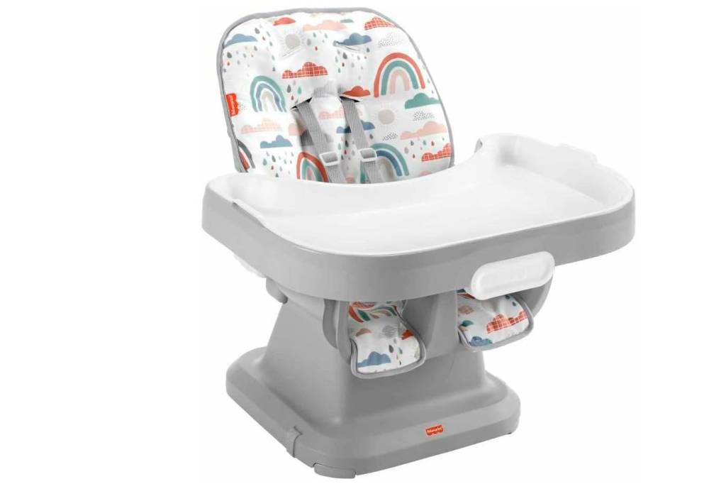cadeira-de-alimentação-portátil-e-compacta Cadeirinha de alimentação para colocar sobre a cadeira. É branca e cinza. O assento branco tem desenhos coloridos, como nuvens e arco-iris.