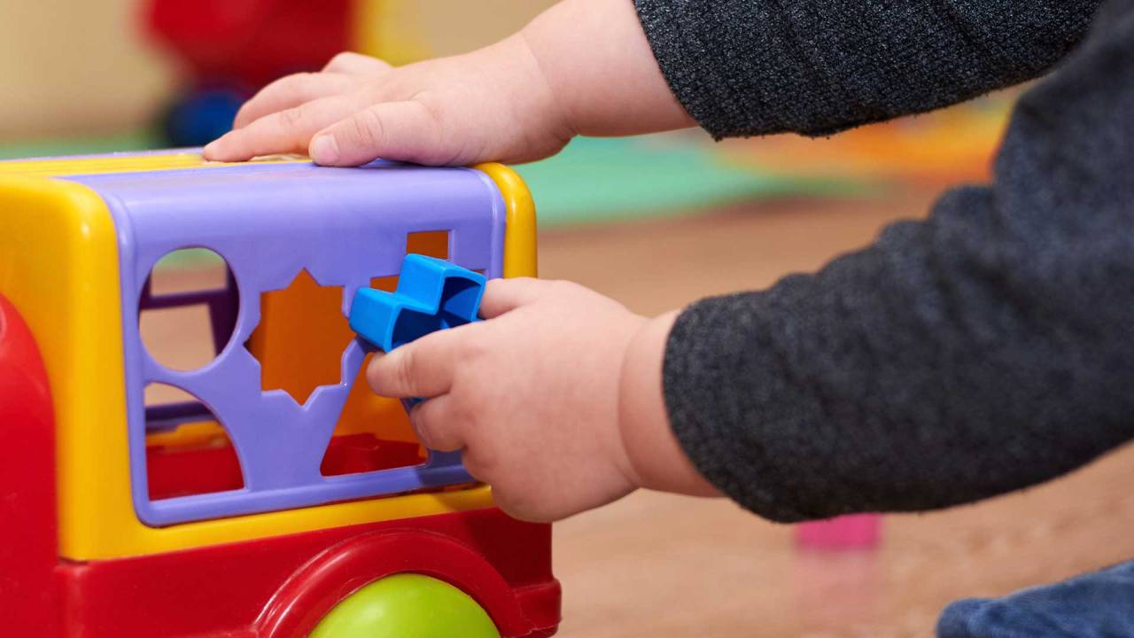 close na mão de uma criança colocando uma peça em um brinquedo colorido de encaixe