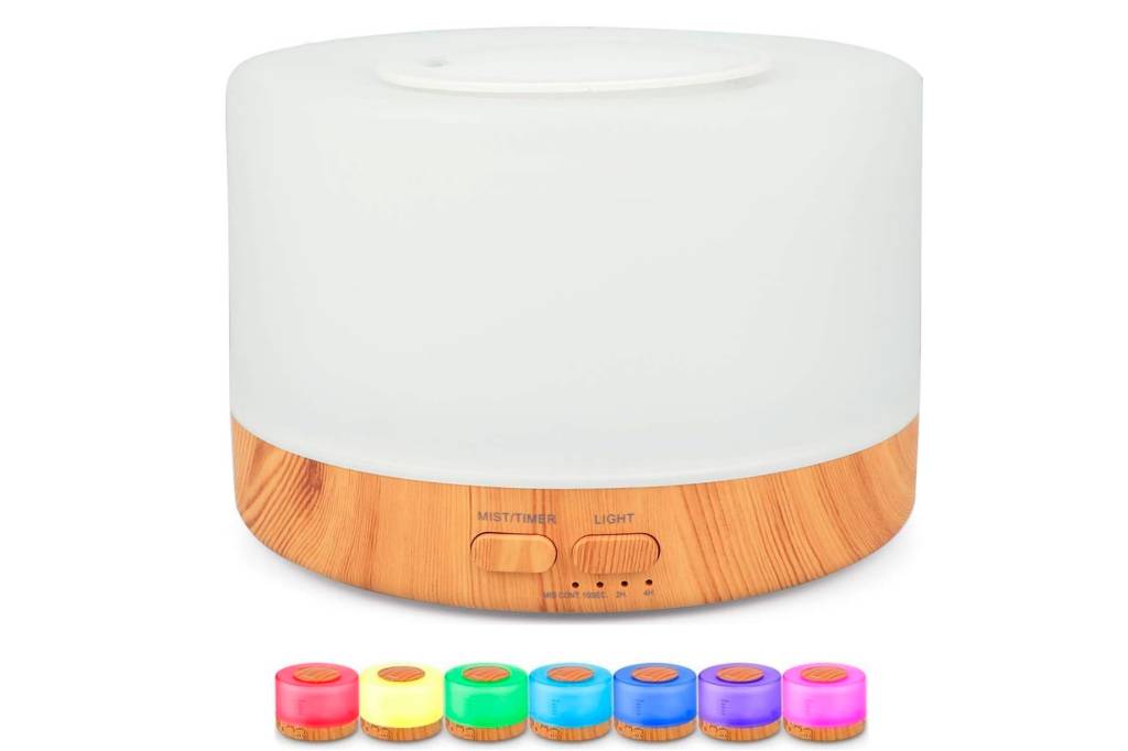difusor-aromatizador-de-ambientes Sobre fundo branco, o aromatizador é redondo, branco com base de madeira clara. Na parte de baixo da imagem, estão enfileirados exemplos das cores que ele fica, em miniatura. Da esquerda para a direita: vermelho, amarelo, verde, turquesa, azul, roxo e rosa.