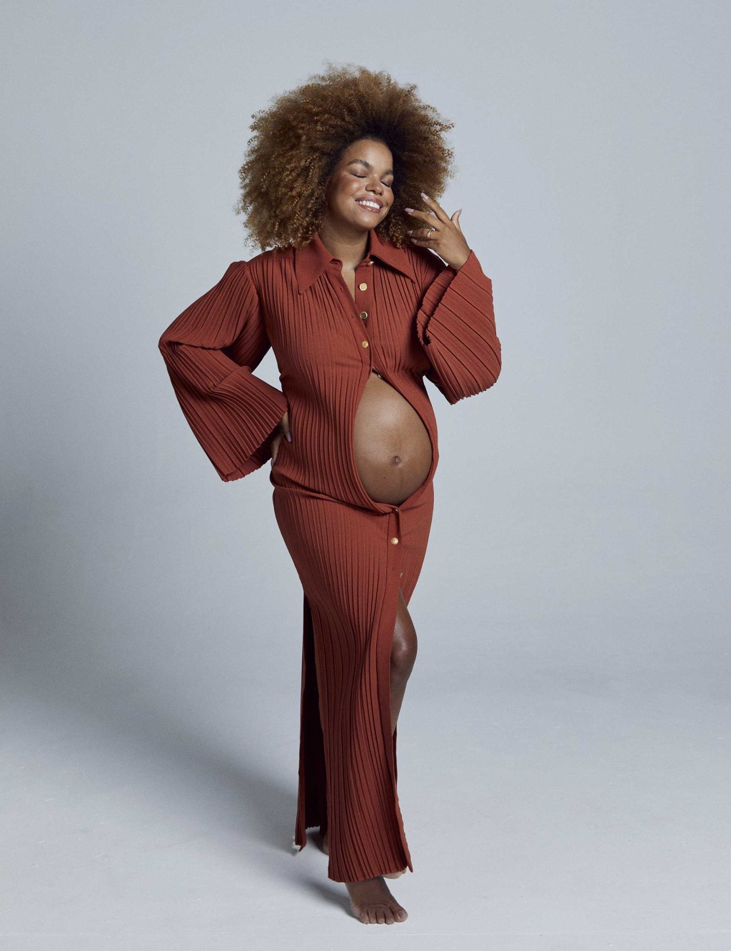 Mulher grávida usando um vestido que deixa a barriga à mostra. Ela sorri, olhando levemente para o lado