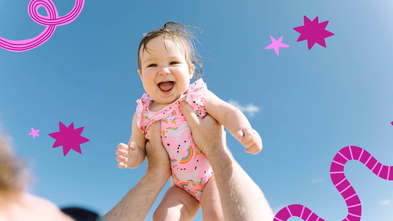 Pai ergue filha sorridente para o alto. O céu está azul