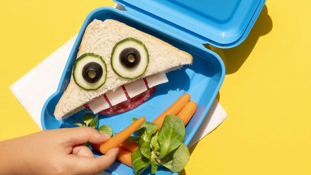 pão e legumes dispostos em um recipiente de plástico de modo que formam um rosto com boca