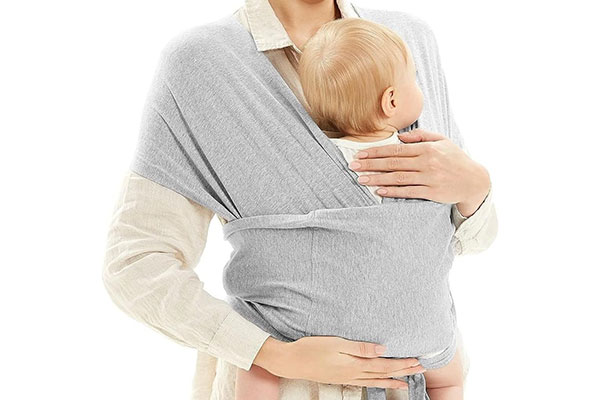 Mulher segurando um bebê que está envolto em um tecido, preso nos ombros e em torno da mãe