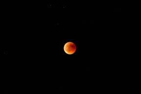 Horizontal long shot of an orange and red moon in the dark sky at night eclipse lua lunar